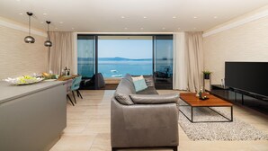 Un salon moderne avec un canapé, une table basse et un téléviseur. Il est doté d’une grande fenêtre offrant une vue sur la mer et d’un balcon.