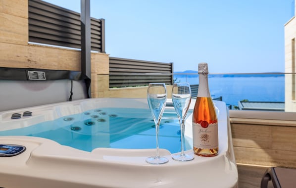 Ein Whirlpool mit zwei Sektgläsern und einer Weinflasche, mit Blick auf ein Gewässer.