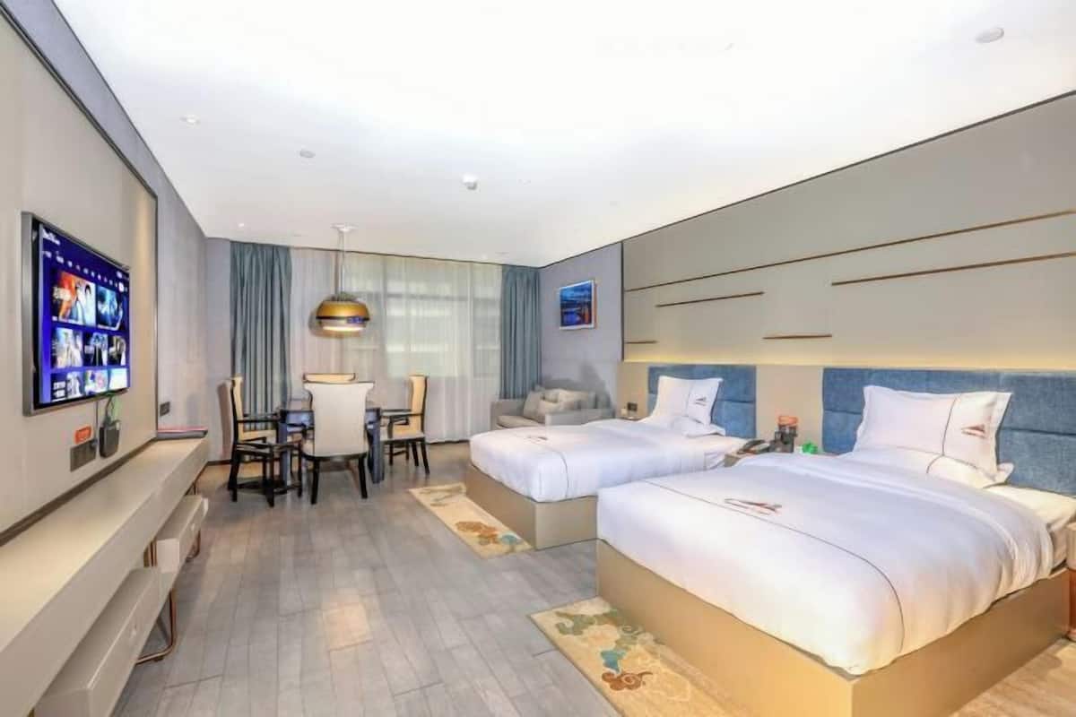 A hotel room with two beds, a desk, a TV, and a large window.