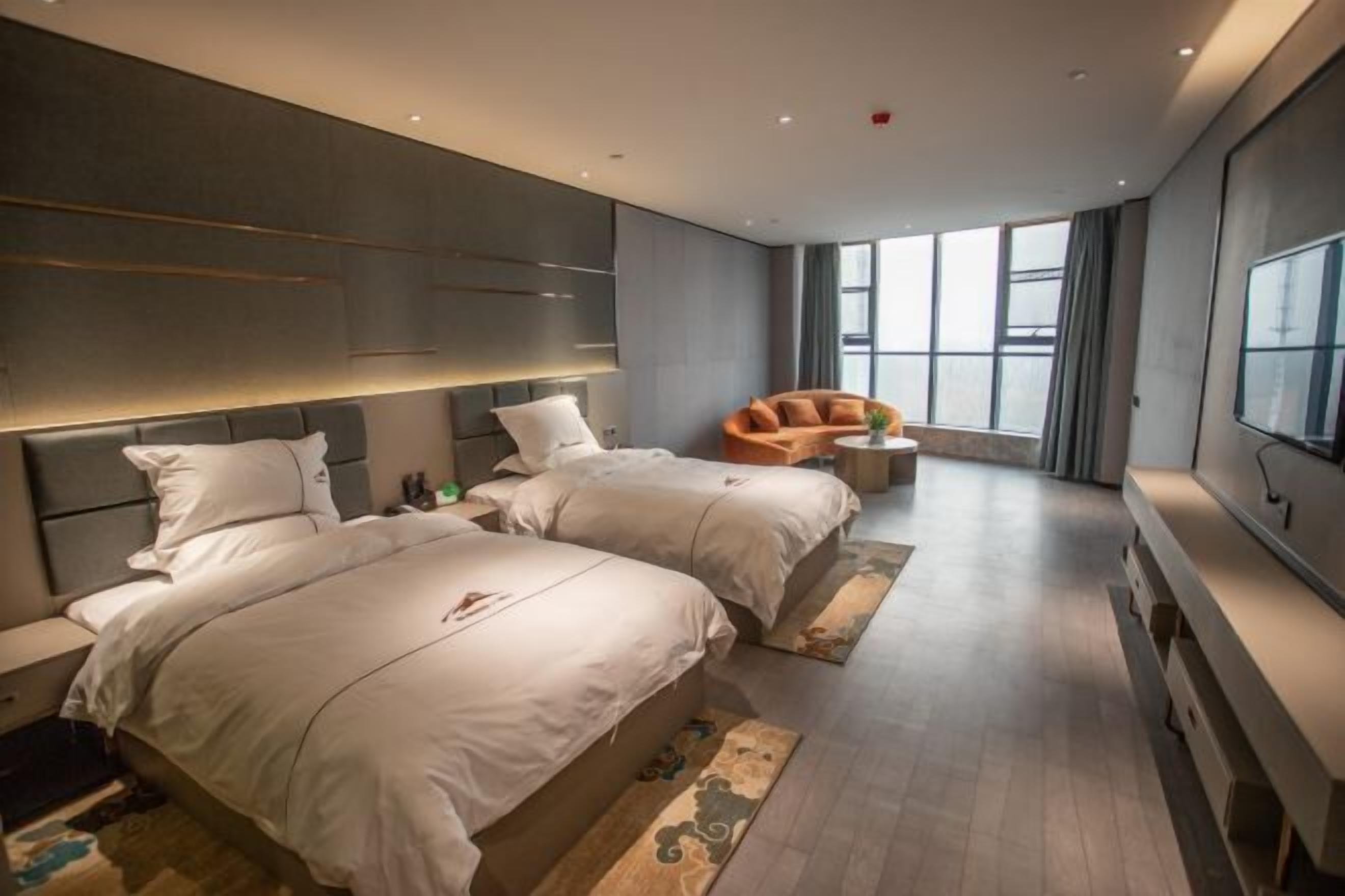A modern hotel room with two beds, a sofa, a TV, and large windows.