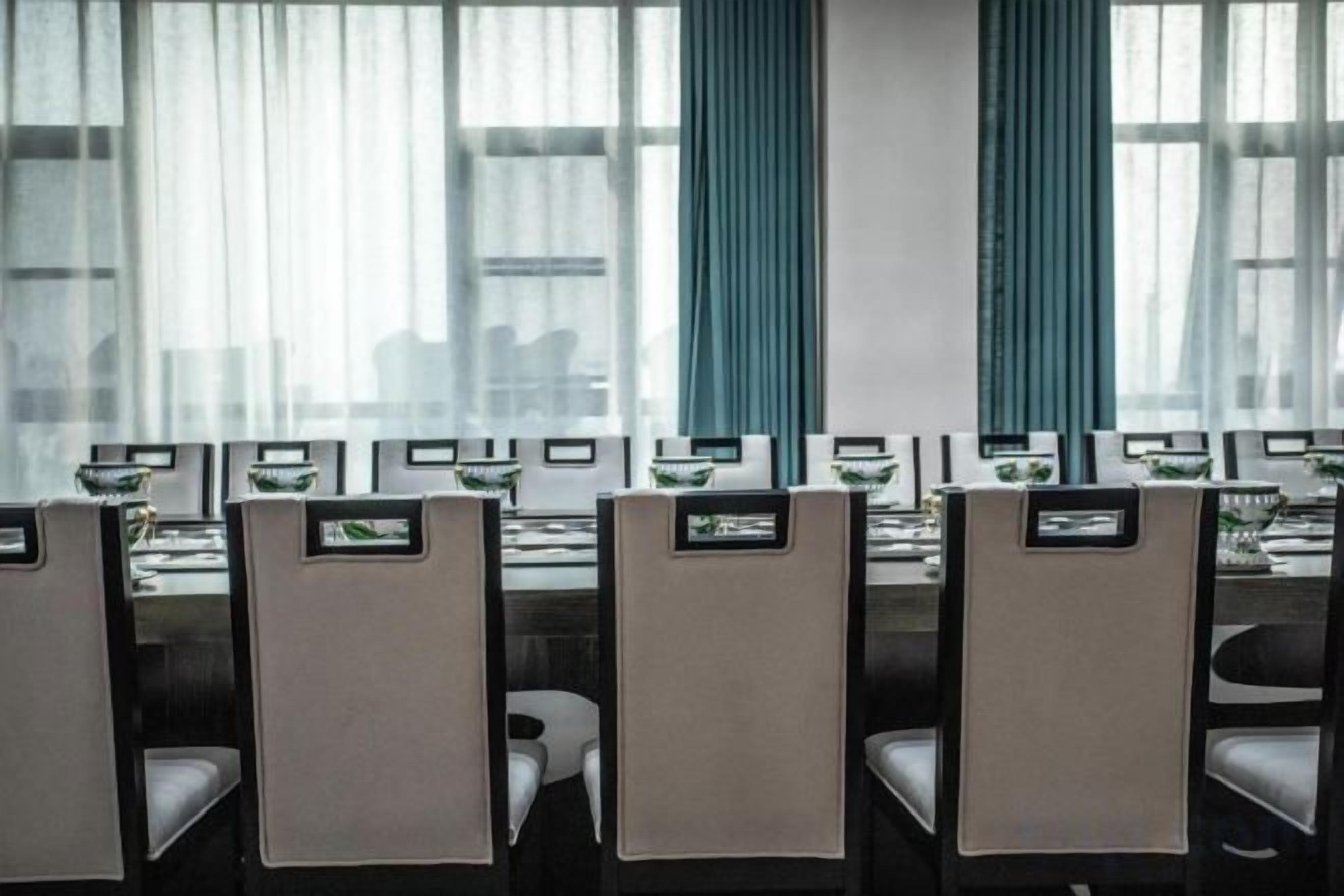 A conference room with rows of tables and chairs, large windows with curtains, and a view of the cityscape.