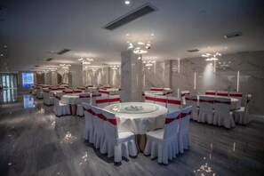 Un salón de banquetes con mesas redondas, sillas blancas y cintas rojas.