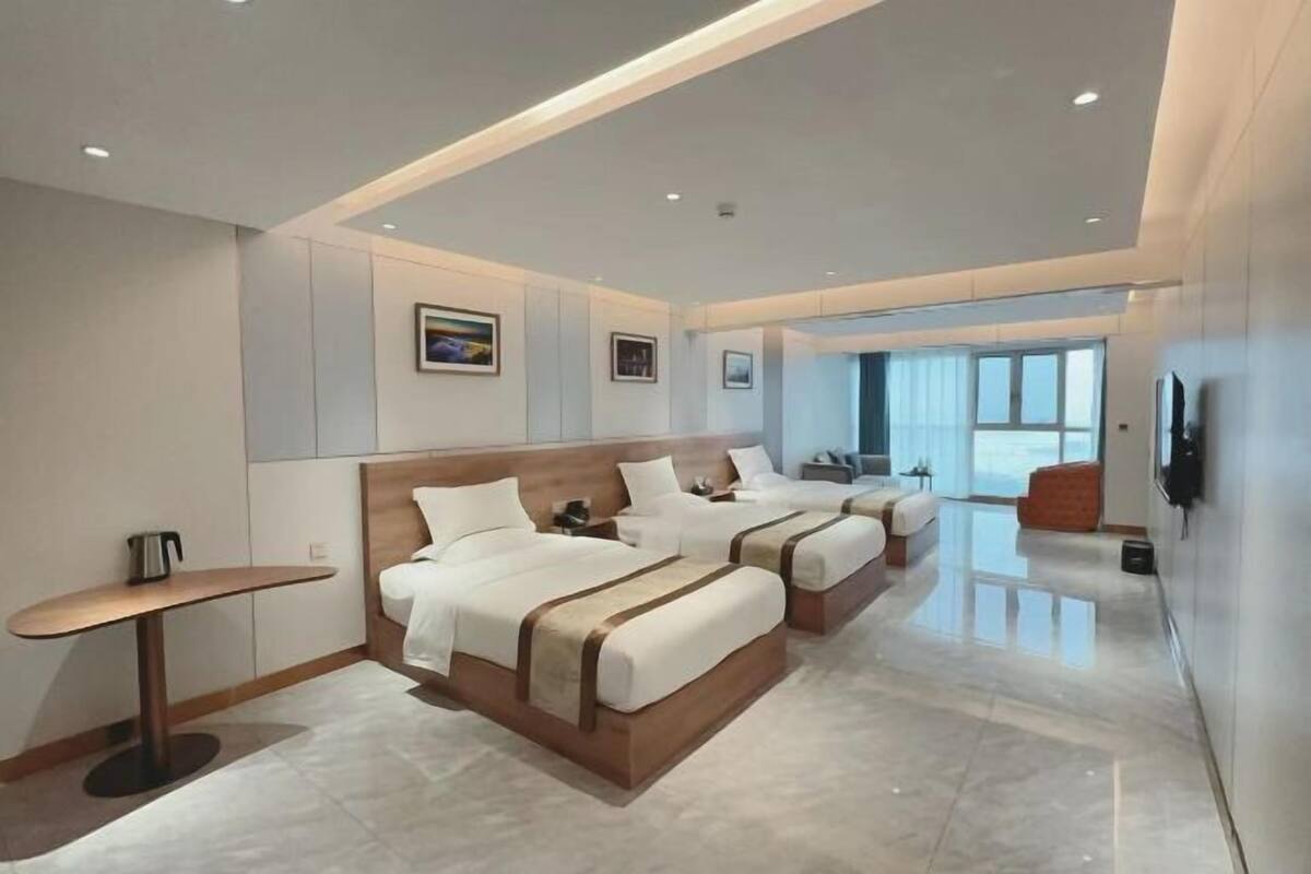 A hotel room with three beds, a small table, and a TV.