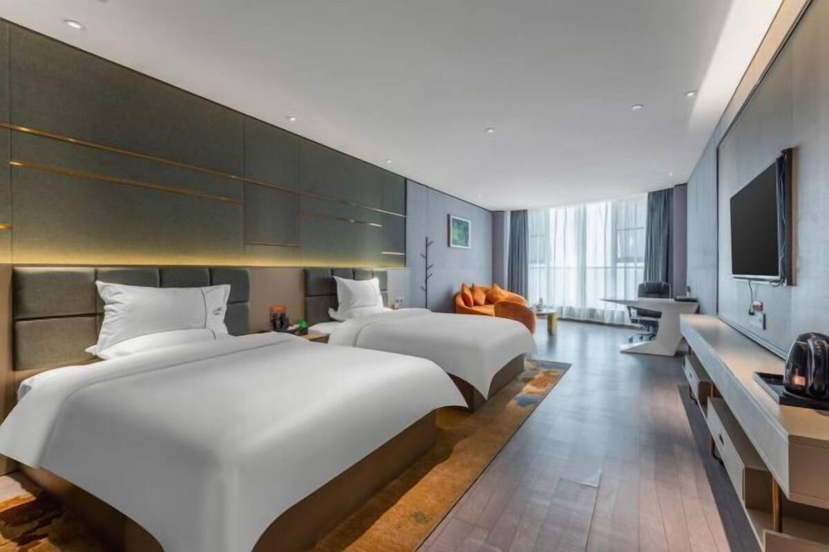 A modern hotel room with two beds, a seating area, and a large TV.