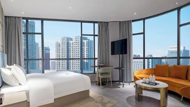 A hotel room with a large bed, a sofa, a TV, and a view of tall buildings. - Danjiangkou Guanlan International Hotel（Hanjiang Avenue storefront） (Danjiangkou)