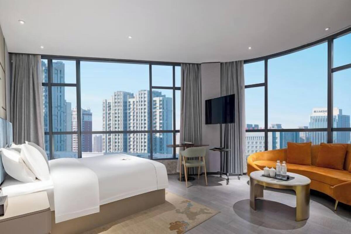 A hotel room with a large bed, a sofa, a TV, and a view of tall buildings.