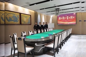 Un salón de conferencias con mesa de billar verde, sillas blancas y una pantalla grande mostrando texto.