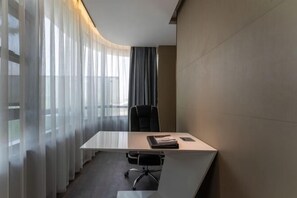 Een moderne vergaderruimte met een witte tafel, een zwarte bureaustoel en een groot raam met dunne gordijnen.