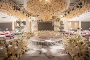 Un salón de banquetes con una mesa redonda central, rodeado de arreglos florales blancos y mesas dispuestas para un evento formal.
