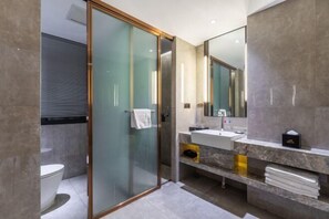 Een moderne badkamer met een douchecabine van glas, een wit toilet, een wastafel met een marmeren blad en een grote spiegel.