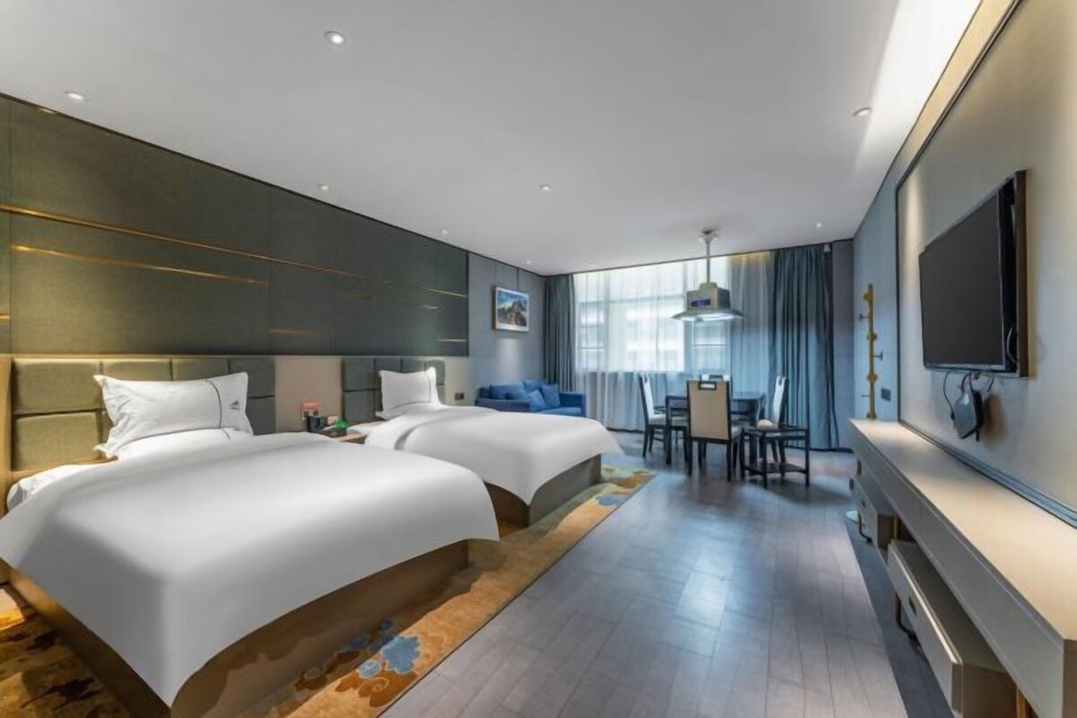 Een moderne hotelkamer met twee bedden, een eethoek en een grote televisie.
