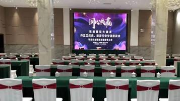 A conference room with rows of tables and chairs, a large screen at the front, and a stage.