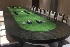 Una mesa de conferencias con sillas, una alfombra verde y algunos objetos sobre la mesa.