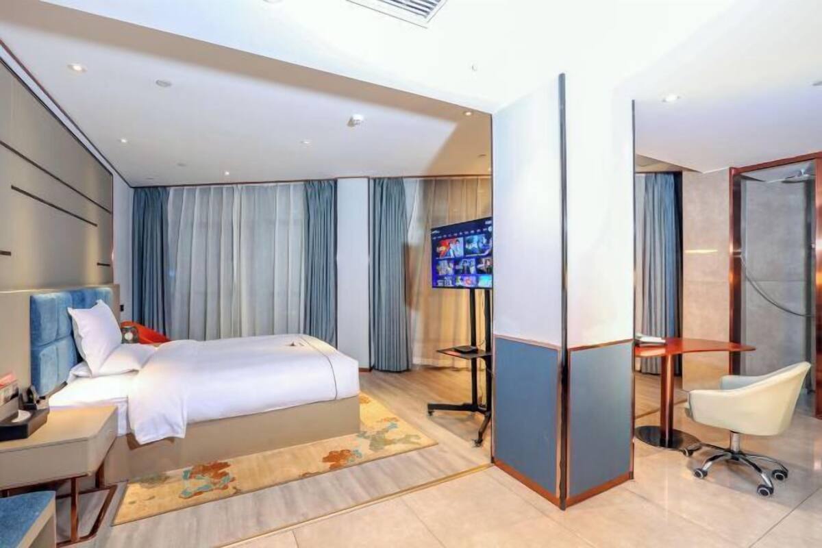 A modern hotel room with a large bed, a desk, a chair, and a television.