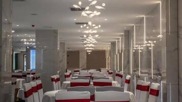 A hotel conference room with rows of tables and chairs, each with a red and white chair cover.