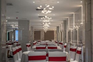 Un salón de conferencias de hotel con filas de mesas y sillas, cada una con una funda roja y blanca.