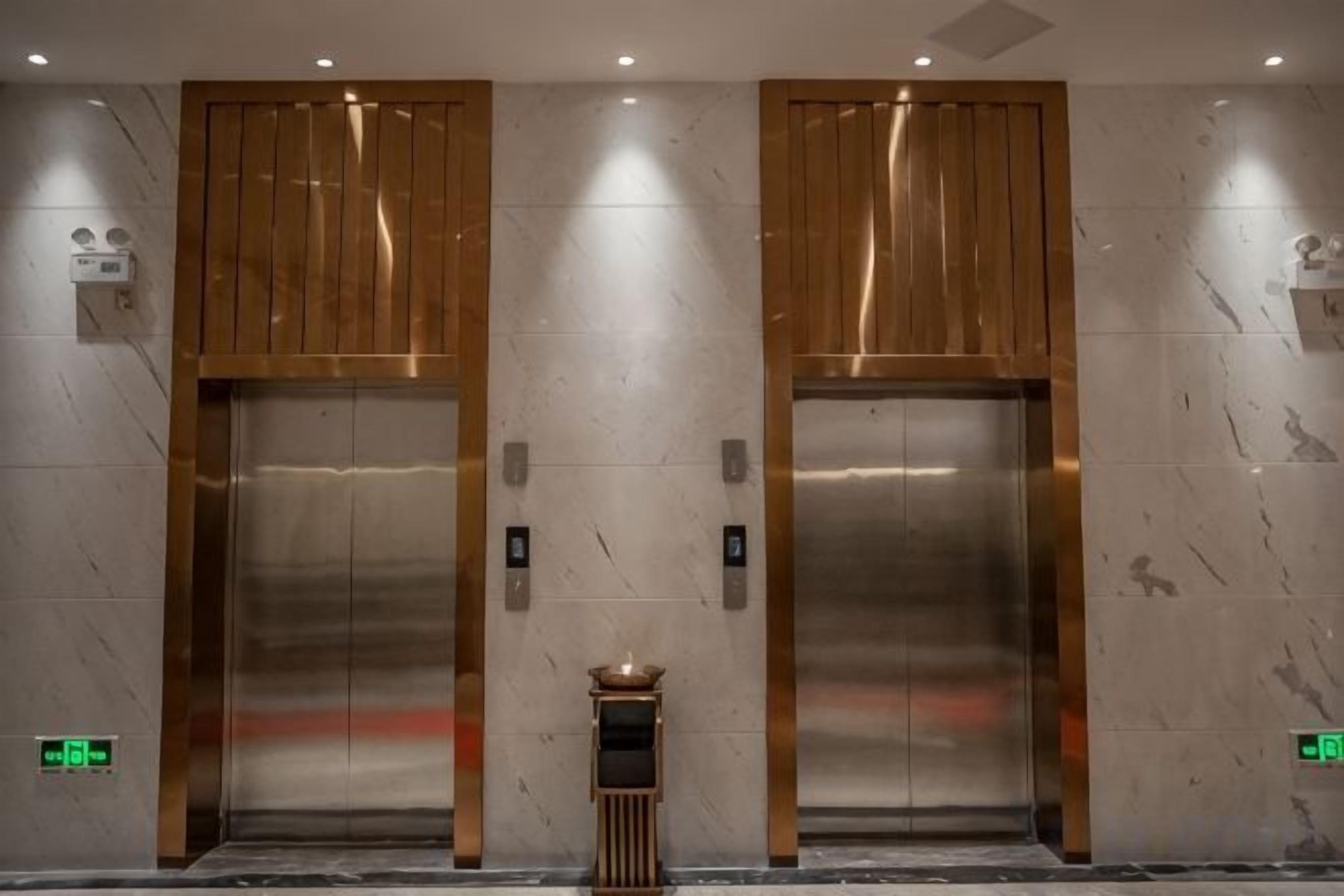 Dois elevadores com portas metálicas, uma pequena mesa e um sinal de saída de emergência fixado na parede.