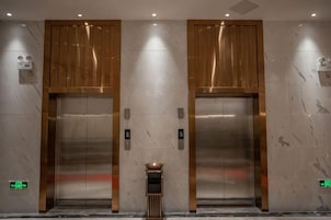 Two elevators with metallic doors, a small table, and a wall-mounted emergency exit sign.