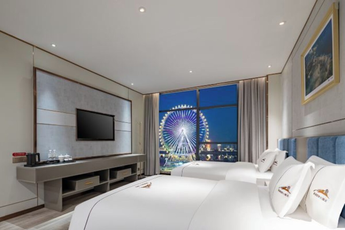 Una habitación de hotel moderna con una cama grande, un televisor de pantalla plana, un escritorio con ordenador y vistas a una noria nocturna.