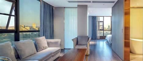 Una habitación de hotel moderna con sofá, sillones, una mesita de madera y ventanas amplias con vistas a la ciudad.