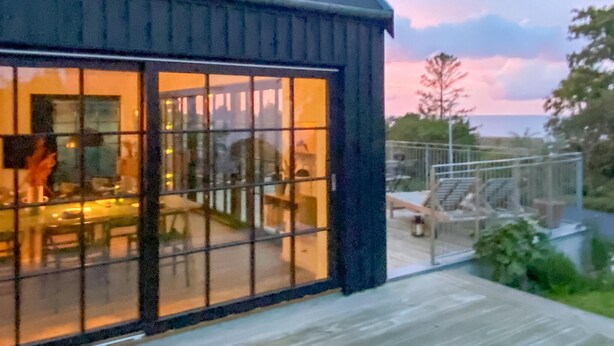 Een modern huis met grote ramen, een terras en buiten zitplaatsen.