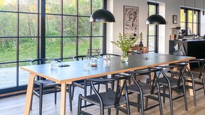 Een moderne eetruimte met een lange tafel, zwarte stoelen en hanglampen.