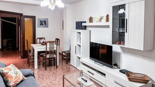 Un salon moderne doté d’un téléviseur à écran plat, de meubles blancs et d’un coin repas avec une table et des chaises.