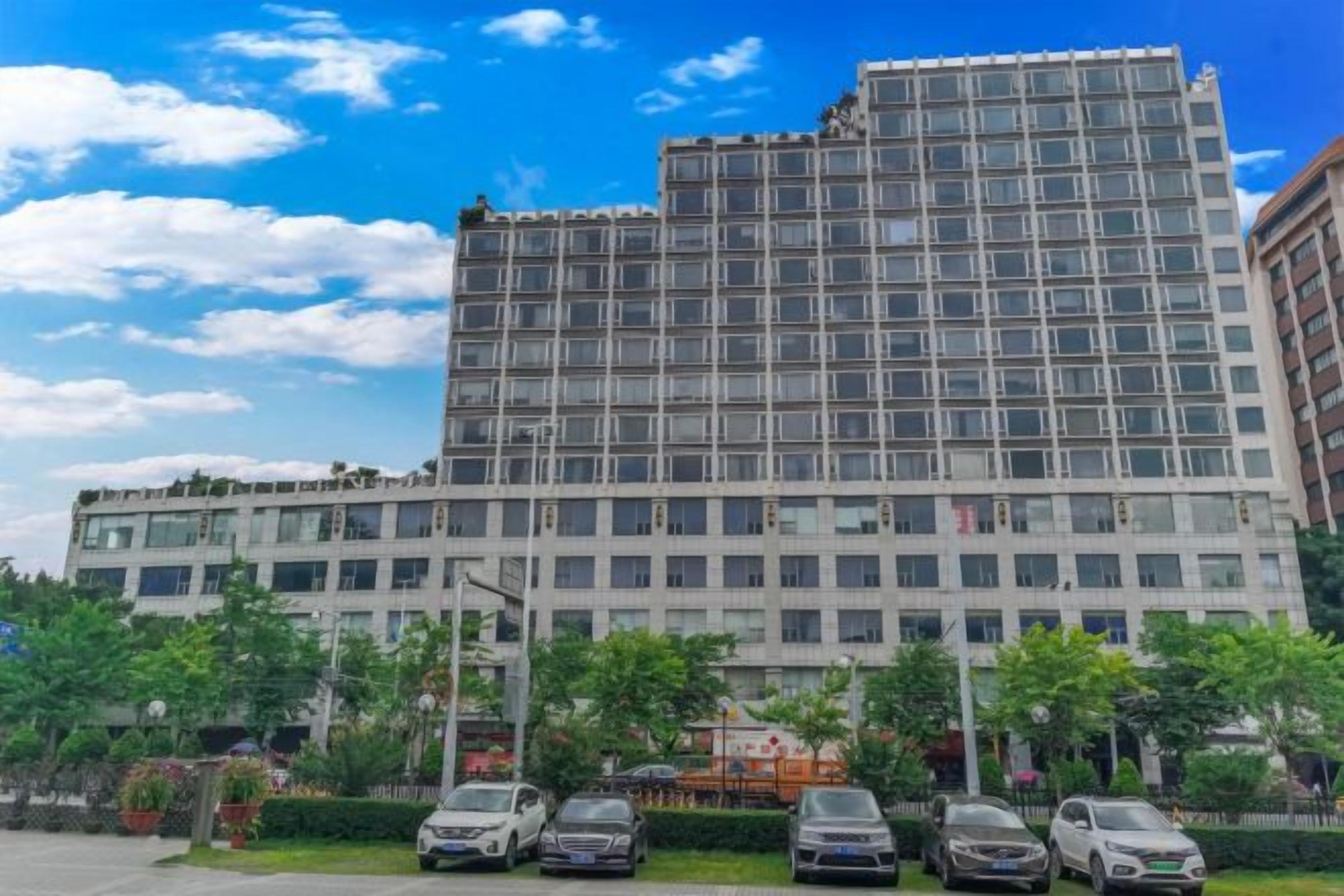 A multi-story hotel with a modern facade, several parking spaces, and a clear sky.