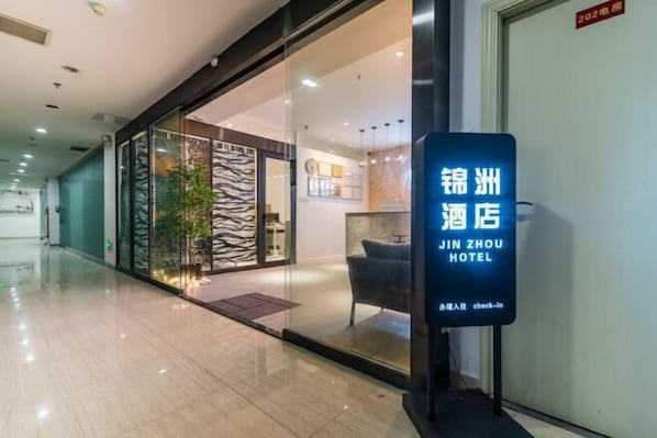 A hotel entrance with a glass facade, a reception desk, and a sign indicating the hotel name.