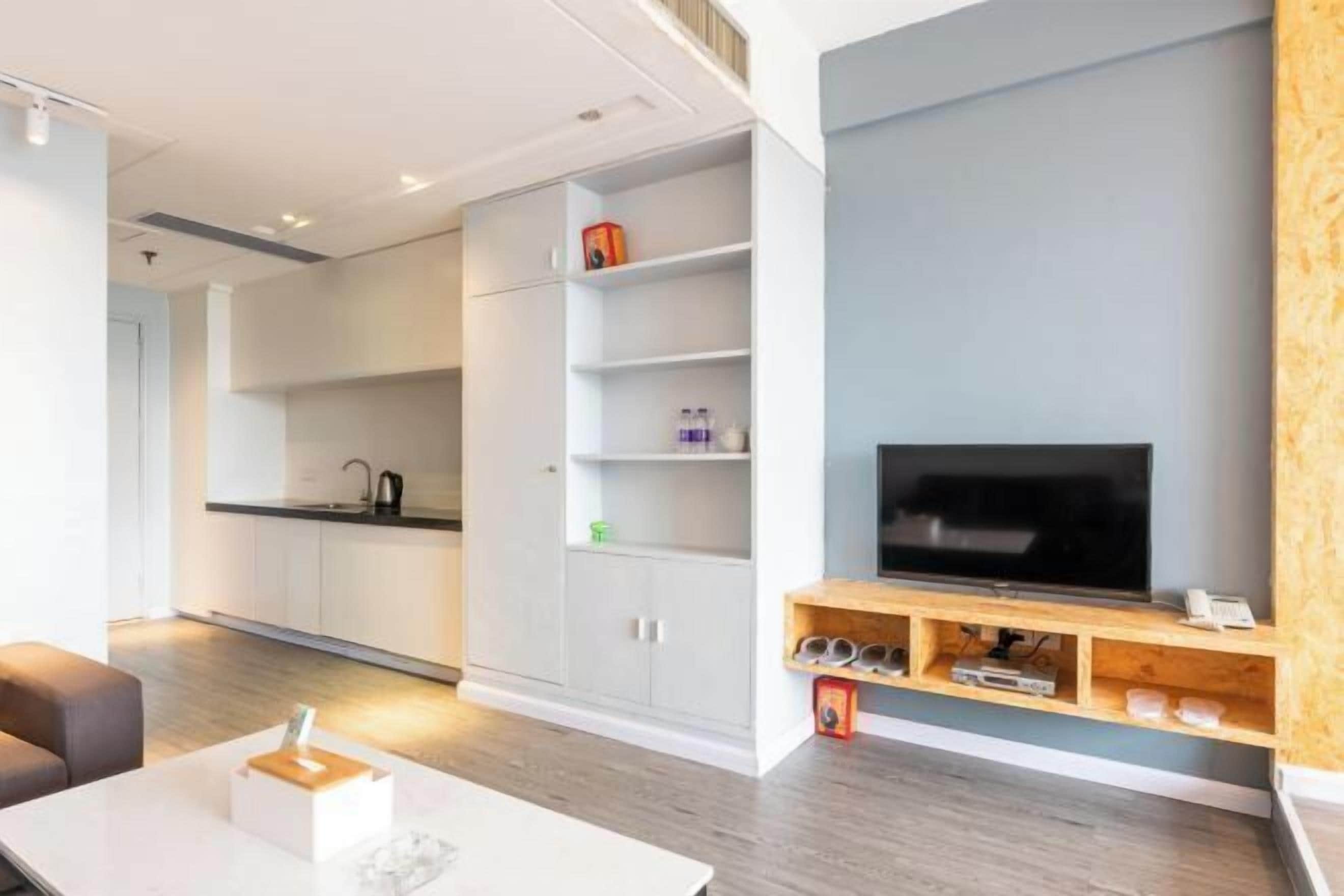 A modern living room with a flat-screen TV, wooden TV stand, and a built-in shelf unit.