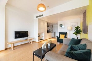 A modern living room with a flat-screen TV, a bench, a sofa, and a dining area in the background.