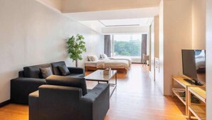 Una sala moderna con un conjunto de sofá, una mesa de centro, un televisor y vistas de un dormitorio con cama y planta.
