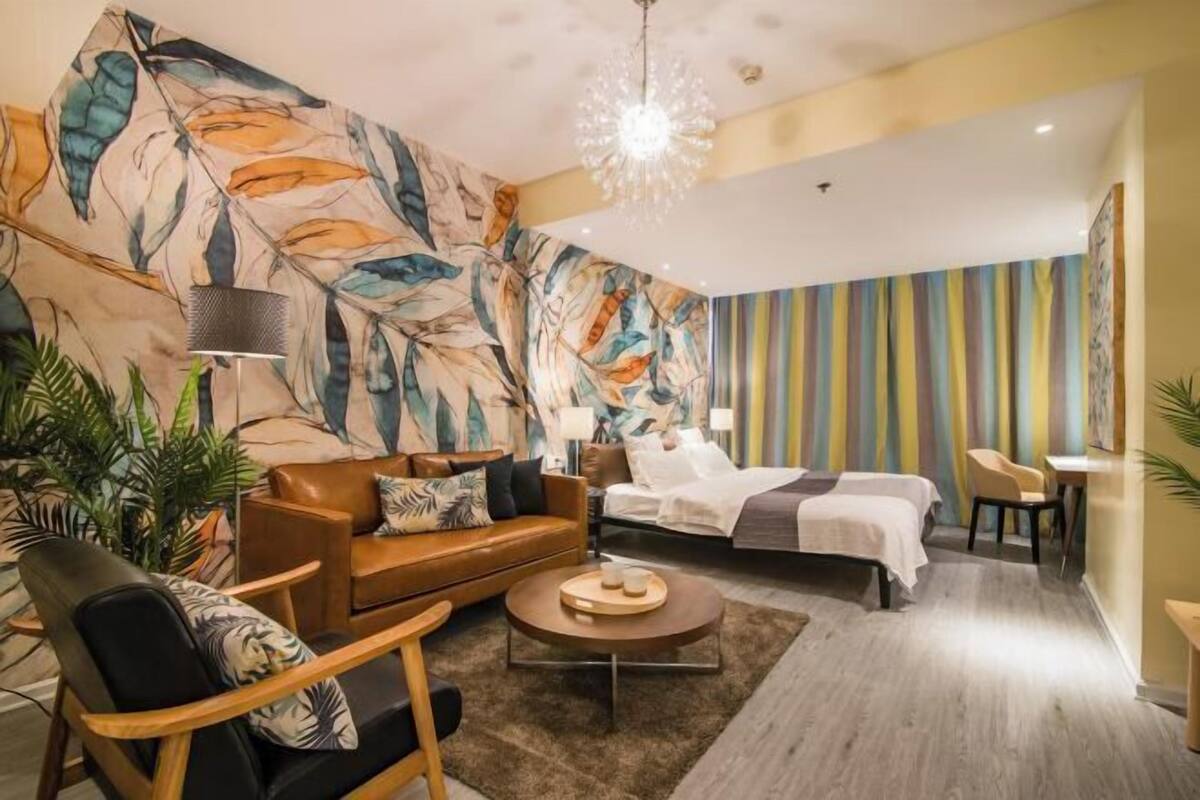 Una habitació d'hotel moderna amb un mural abstracte gran, una zona de seients acollidora, un llit amb cortina a ratlles i una làmpada penjant.
