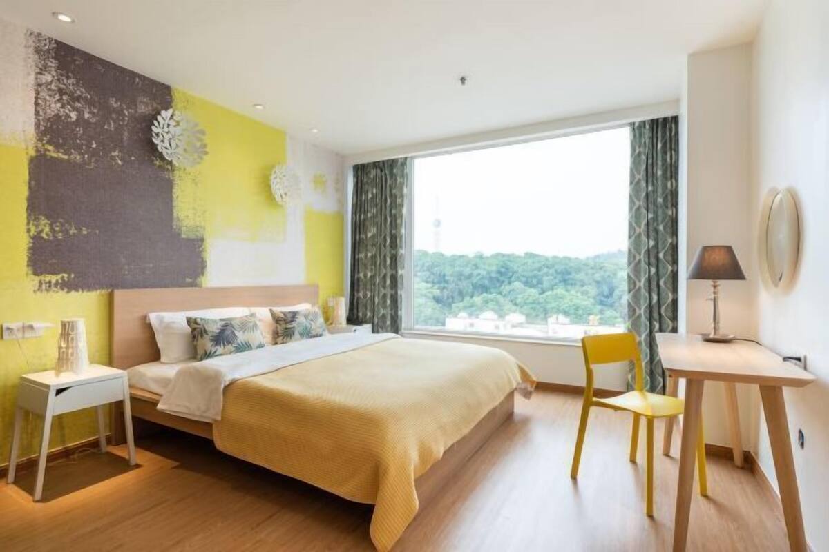 Habitació d'hotel amb llit, escriptori, cadira i finestra gran que dona a zones verdes.