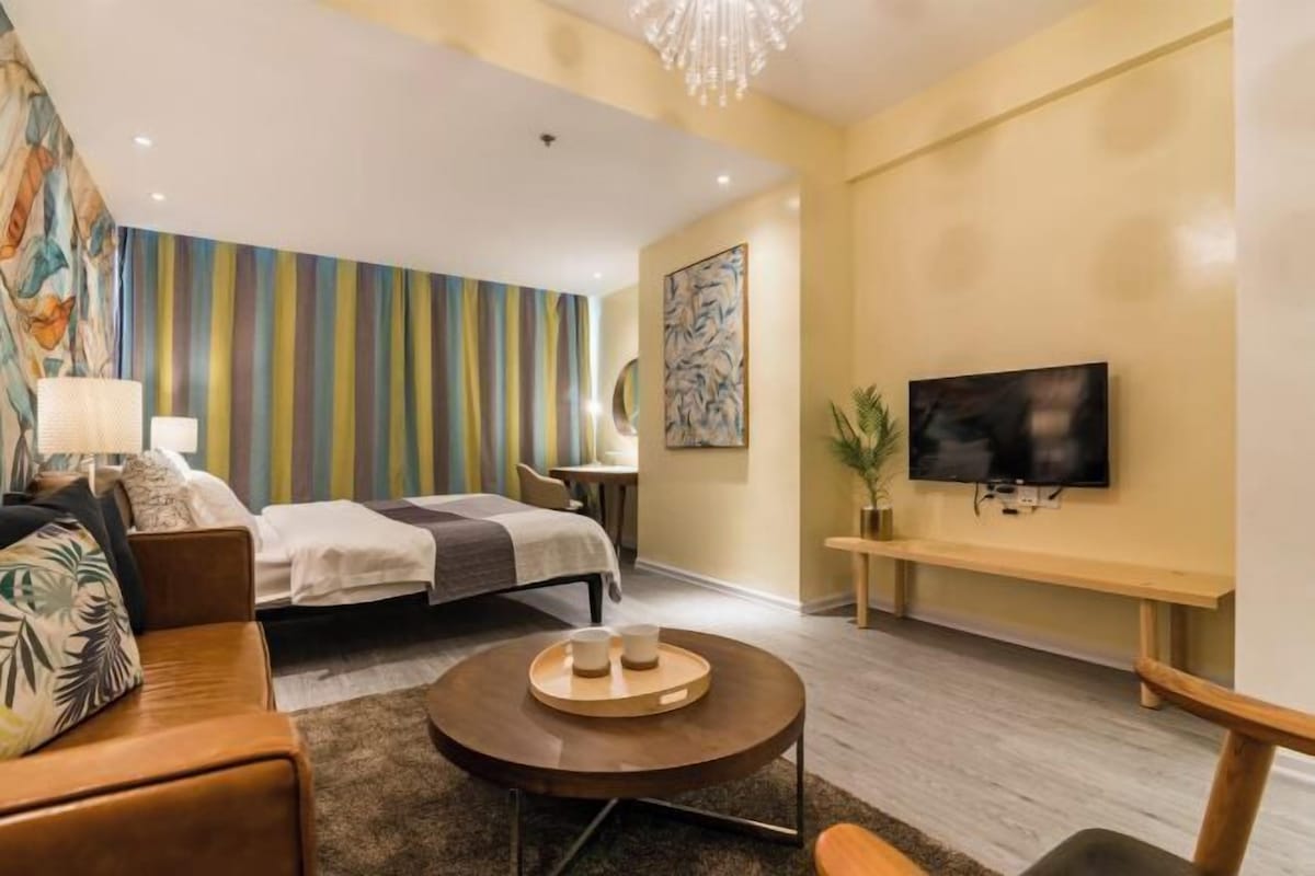 A modern hotel room with a bed, a round coffee table, a TV, and a colorful striped wall.