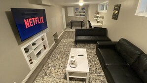 A living room with a flat-screen TV displaying 'NETFLIX', a white coffee table, a black leather sofa, and a patterned rug. - Cute family cottage getaway near Lake Simcoe! (Innisfil)