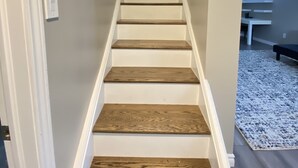 A staircase with wooden steps and white walls, leading to a room with a window and a bench. - Cute family cottage getaway near Lake Simcoe! (Innisfil)