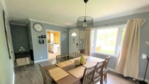A dining room with a wooden table and chairs, a hanging light fixture, and a view of the kitchen through an open doorway. - Cute family cottage getaway near Lake Simcoe! (Innisfil)
