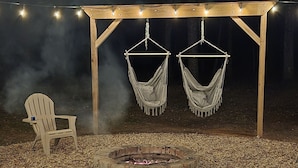 A covered outdoor seating area with a fire pit, two hammocks, and string lights. - Cozy Cabin with a Hot Tub! (Wisconsin Dells)