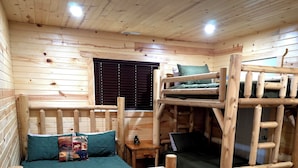 A cabin interior with wooden walls, a bunk bed, a single bed, and a window with blinds. - Cozy Cabin with a Hot Tub! (Wisconsin Dells)