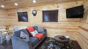 A cozy cabin interior with a sofa, a small table, and a TV mounted on the wall. - Cozy Cabin with a Hot Tub! (Wisconsin Dells)