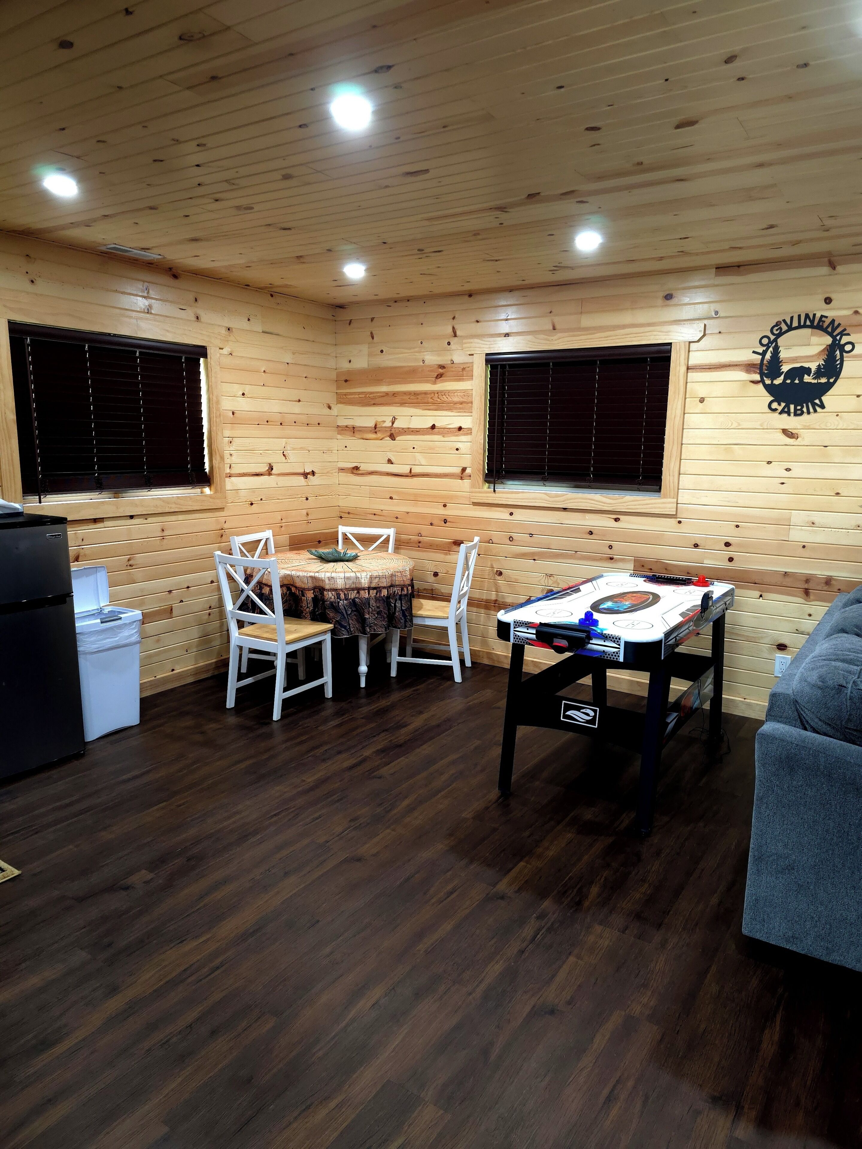 A cabin interior with wooden walls, a dining table with chairs, a pool table, and a sofa.