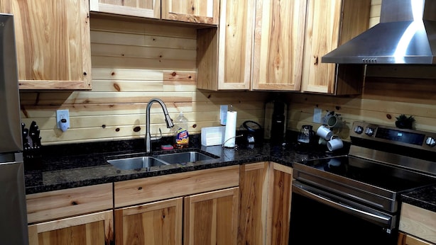 A kitchen with wooden cabinets, a stainless steel range hood, a black stove, and a sink with a faucet. - Cozy Cabin with a Hot Tub! (Wisconsin Dells)