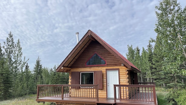 A log cabin with a wooden deck and a red roof, surrounded by trees. - Fireweed Mountain Lodge - Bonzana Cabin (McCarthy)