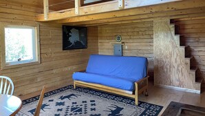 A cabin interior with a loft bed, a dining area, a map on the wall, and a staircase. - Fireweed Mountain Lodge - Bonzana Cabin (McCarthy)
