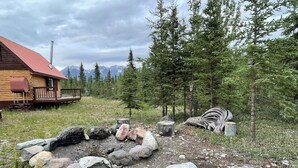 A cabin with a red roof, surrounded by a forest and mountains in the background. - Fireweed Mountain Lodge - Bonzana Cabin (McCarthy)