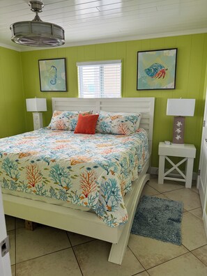 A bedroom with a bed, two bedside tables, a ceiling fan, a window with blinds, and two wall-mounted paintings. - Waterfront island retreat (Placida)