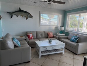A living room with a ceiling fan, a large fish mounted on the wall, a sofa with decorative pillows, a coffee table, and a window with blinds. - Waterfront island retreat (Placida)