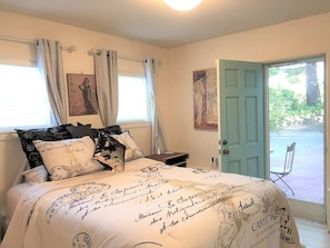 A bedroom with a bed covered in a patterned bedspread, a nightstand, a chair, and a door leading outside.