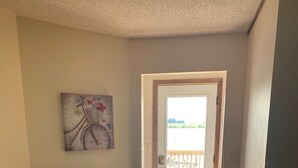 A hallway with a wooden floor, a dark wooden dresser, a framed welcome sign, and a bicycle painting on the wall. - Enjoy Beautiful Sunsets on Lake Reno (Alexandria)